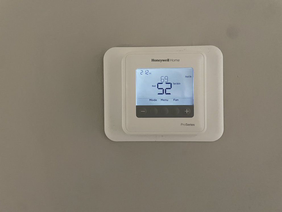 A white thermostat is hanging on a white wall.