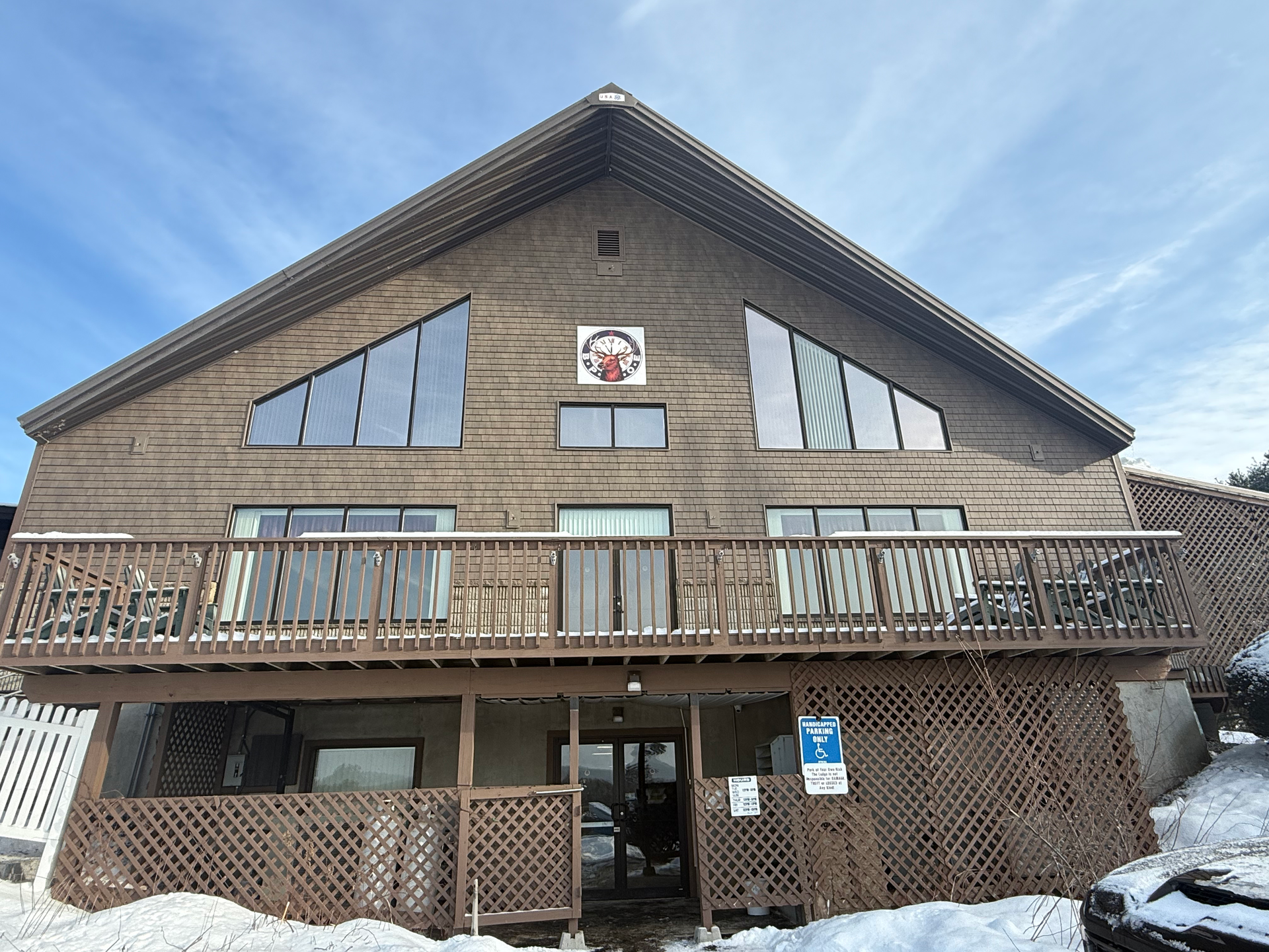 Wooden lodge building with a deck and snow on the ground under a blue sky.