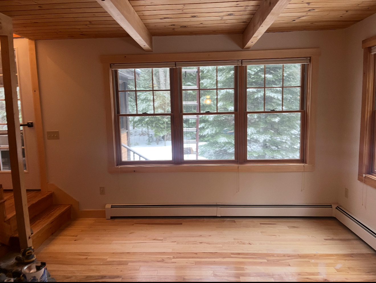 Empty room with wooden ceiling, windows, and floors. White walls and baseboard heaters.