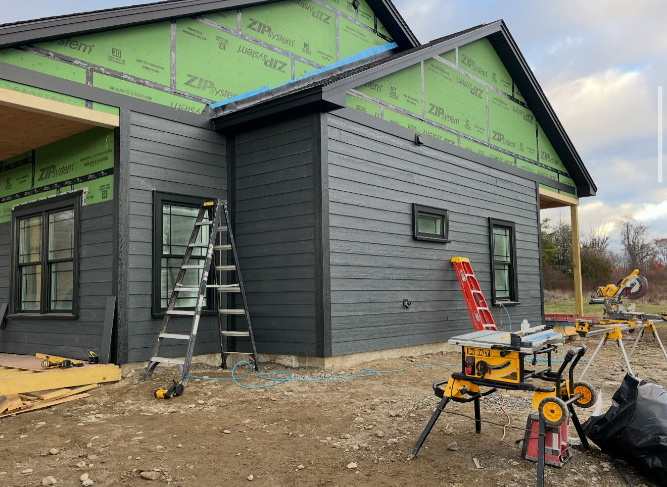 House under construction with dark gray siding, black window frames, and tools.