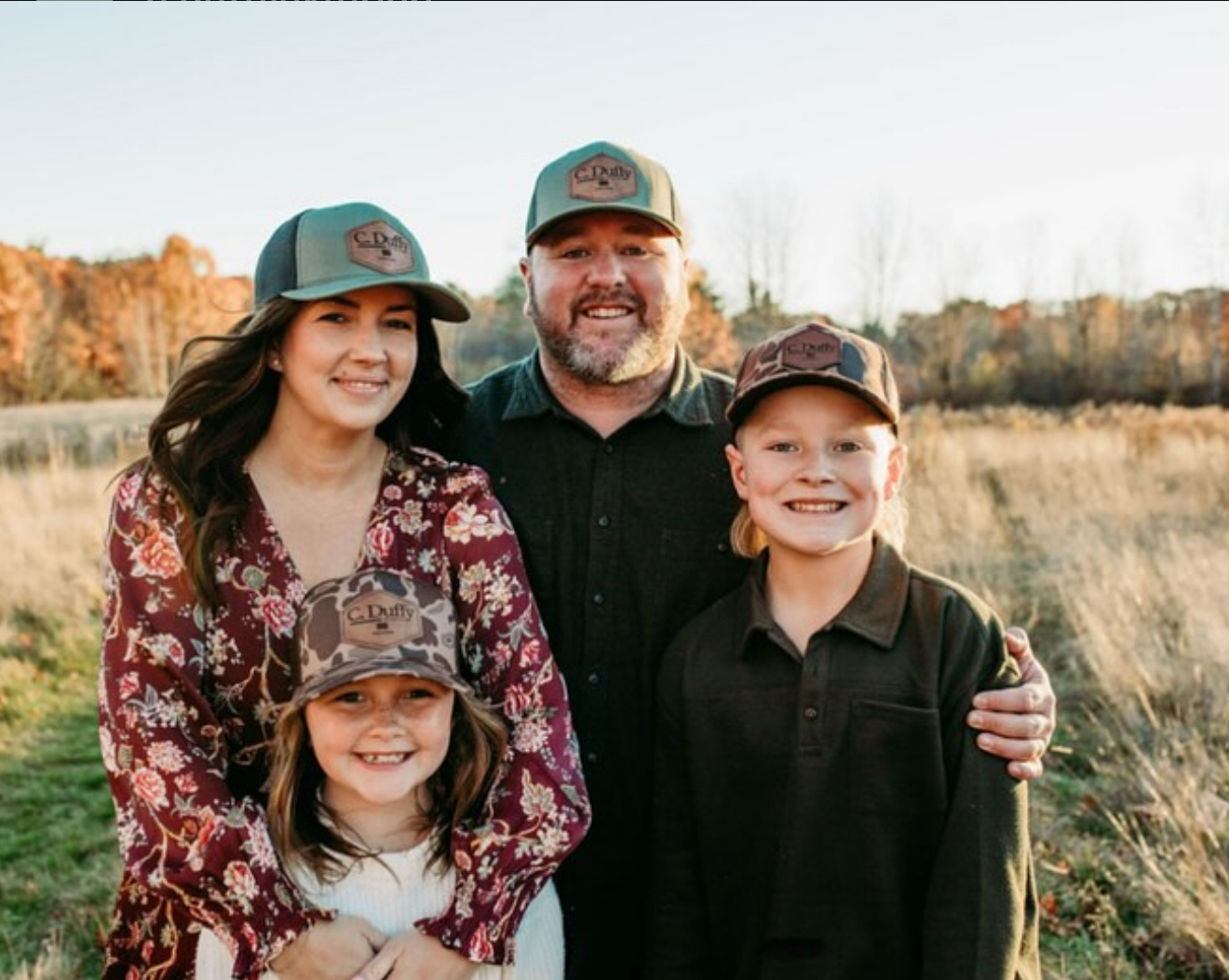 Family of four wearing matching hats, smiling in a field.