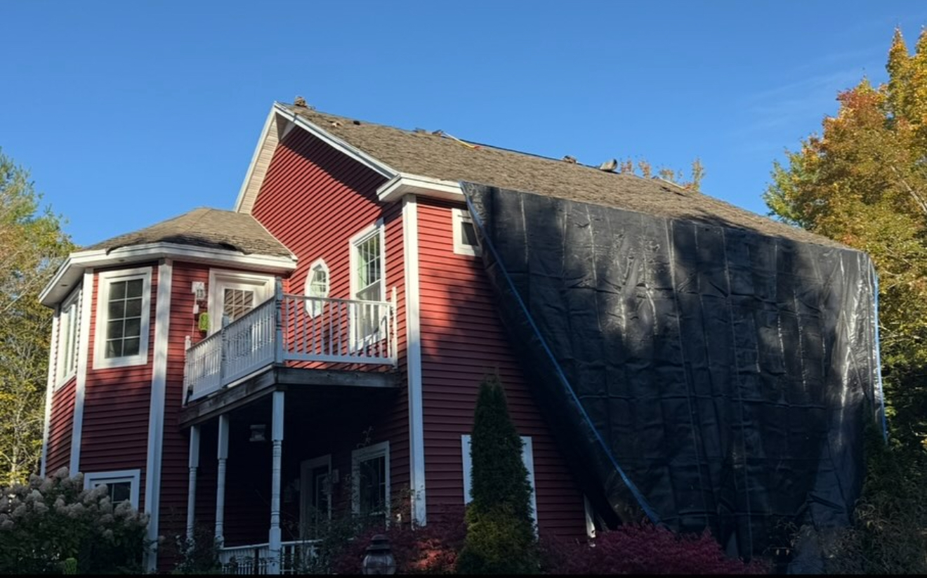 Red house with damaged roof covered by a tarp, sunny day.