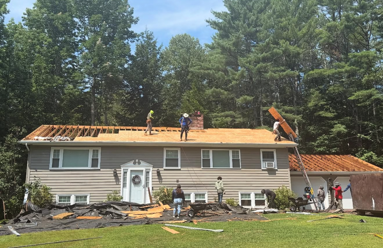 Roofers replacing a roof on a two-story home, with workers on the roof and on the ground.