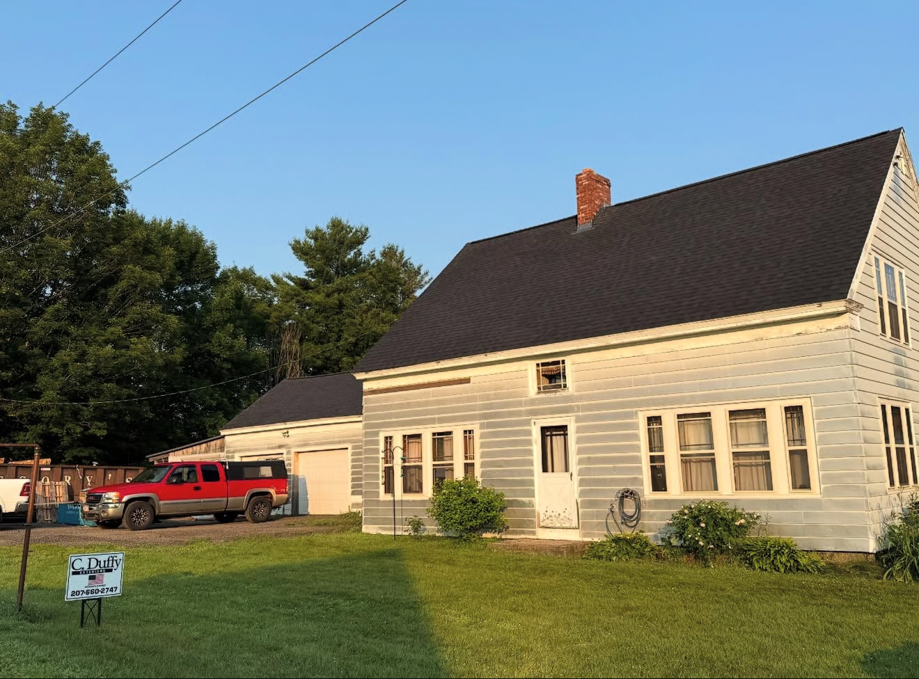 Two-story house with red truck parked beside it on a grassy lot under a blue sky.