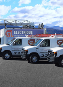 Trois camionnettes blanches sont garées devant un bâtiment sur lequel est écrit « electricque »