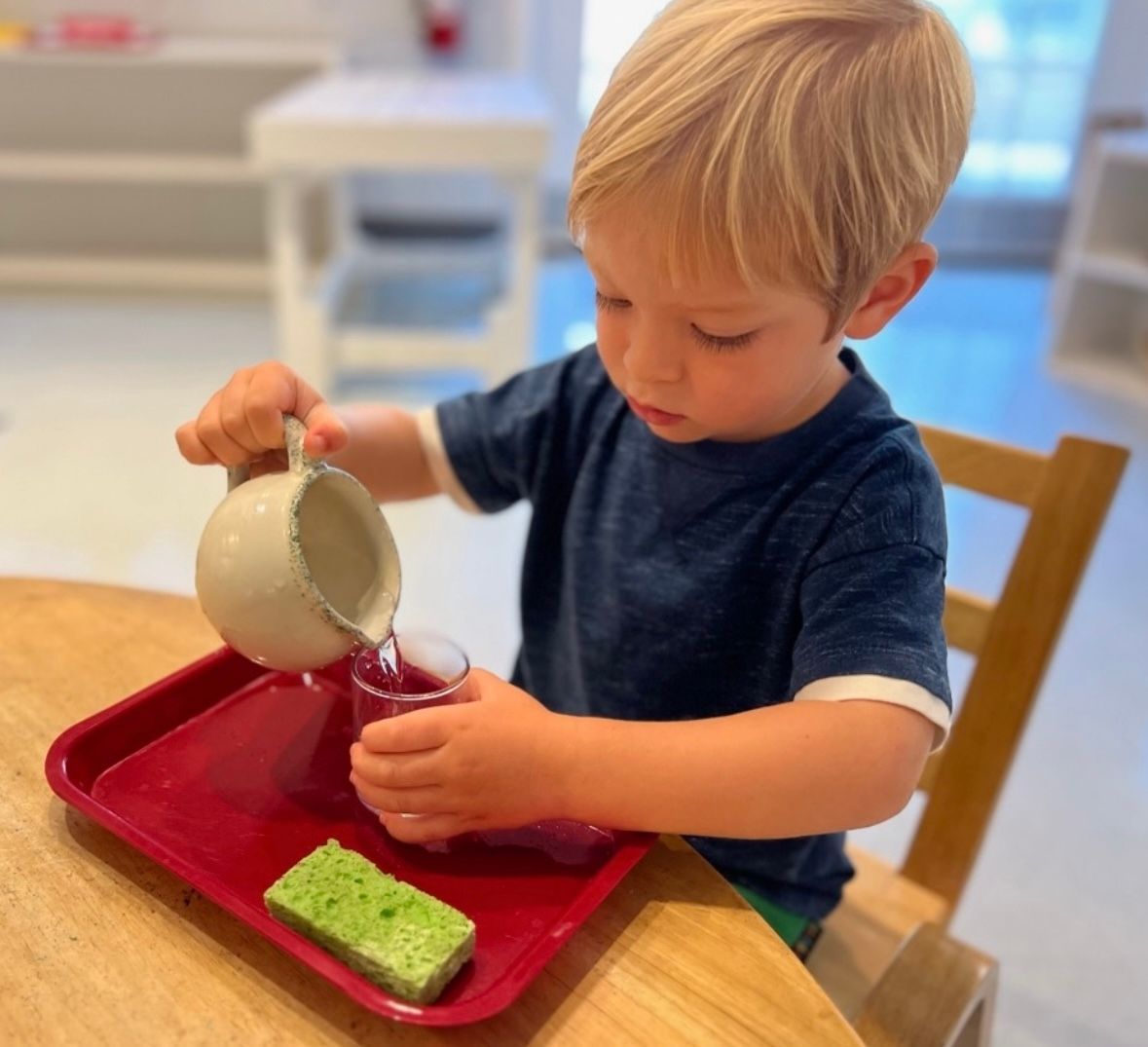 A little boy is pouring something into a cup on a red tray