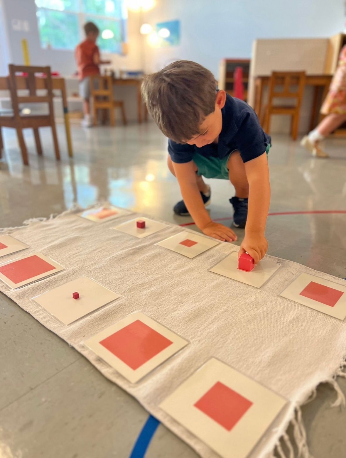 A young boy is playing with red squares on a white cloth.