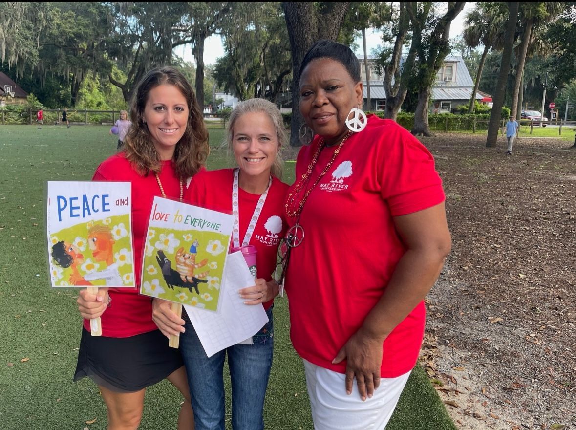 Three women in red shirts are holding signs that say peace