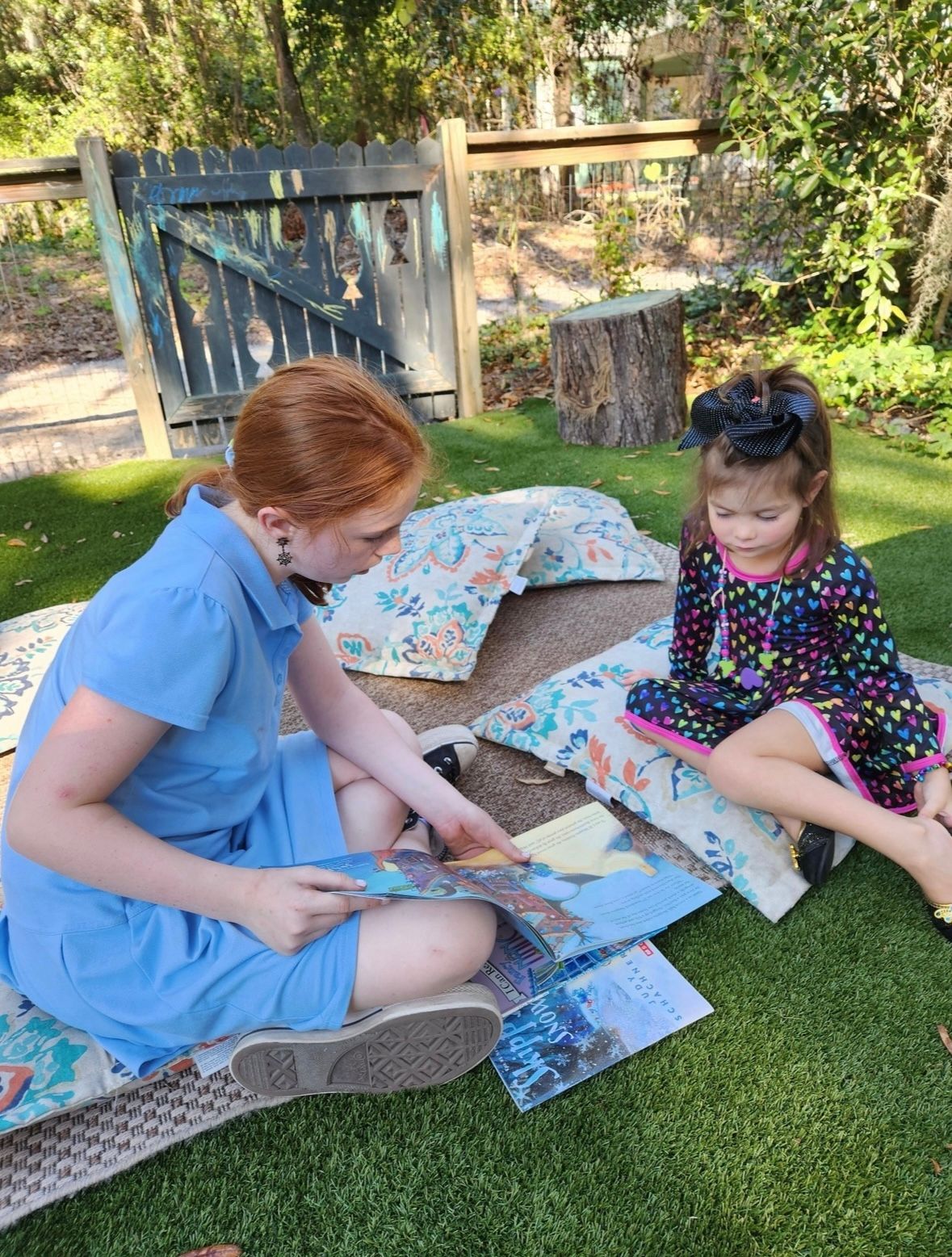 Two young girls are sitting on the grass reading books.