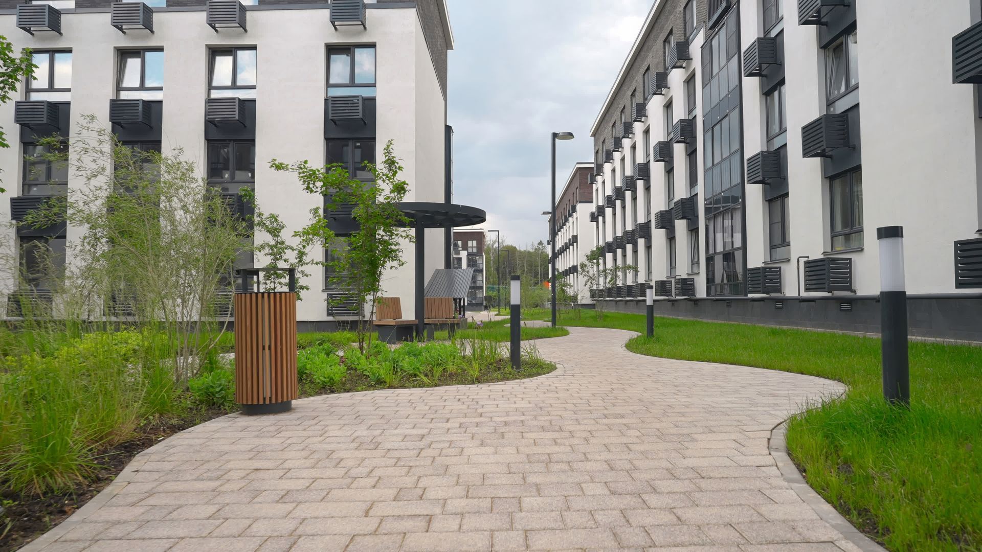 Modern apartment courtyard with paved path, grass, benches, and white buildings on both sides