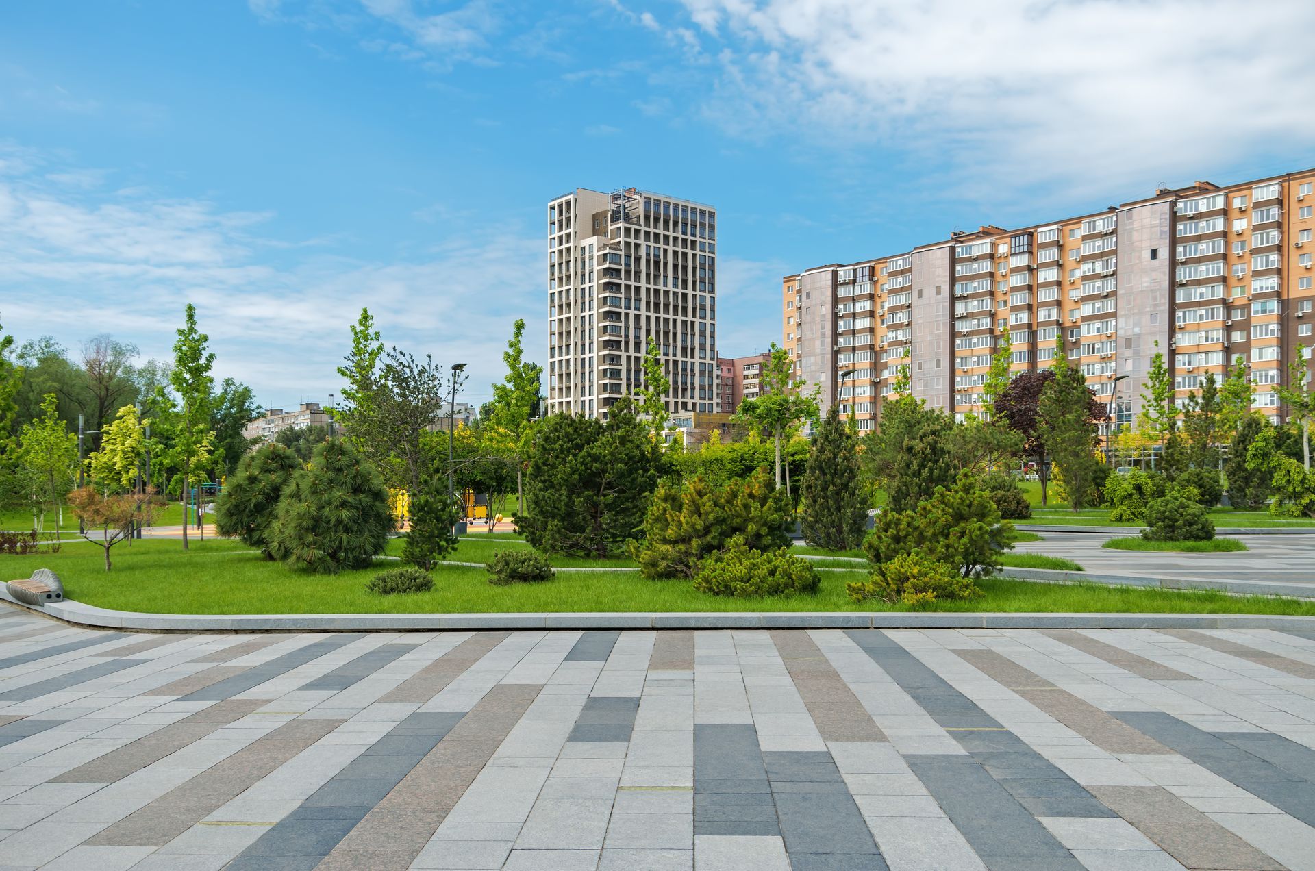 Urban park with green lawn, trees, and tall apartment buildings under a blue sky