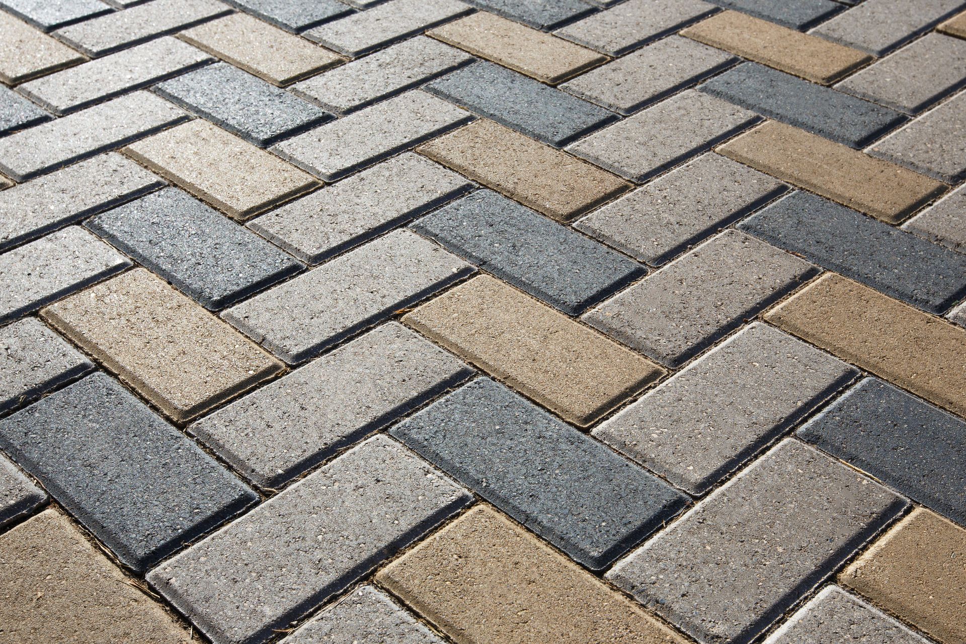 Patterned gray, tan, and beige interlocking paving stones in a herringbone layout.