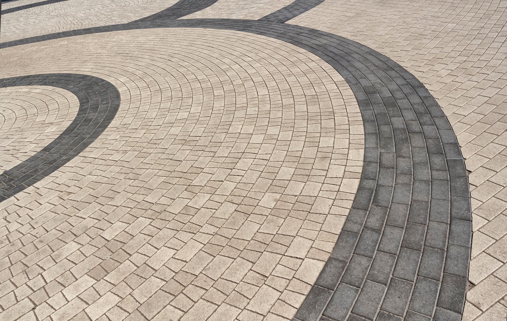Curved gray and beige brick walkway with a sweeping patterned design