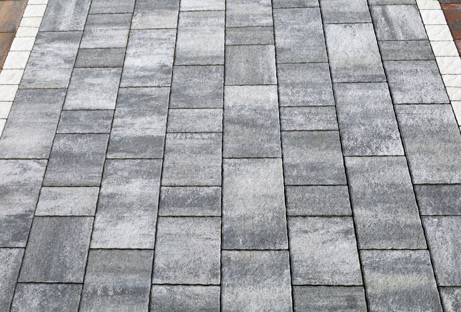 Gray stone paver walkway with a rectangular brick pattern and white edging on both sides
