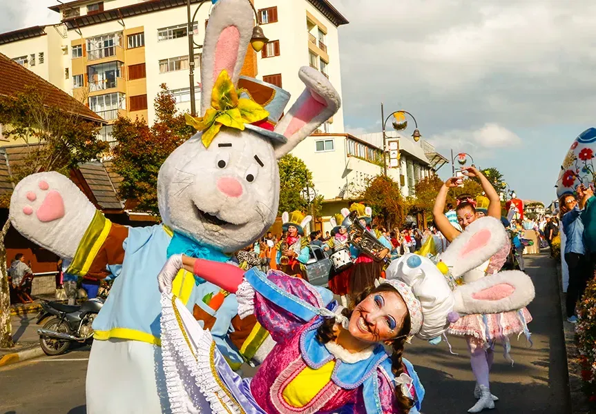 Um artista vestido com uma grande fantasia de coelho e uma mulher com orelhas de coelho dançam em uma rua durante um desfile festivo.