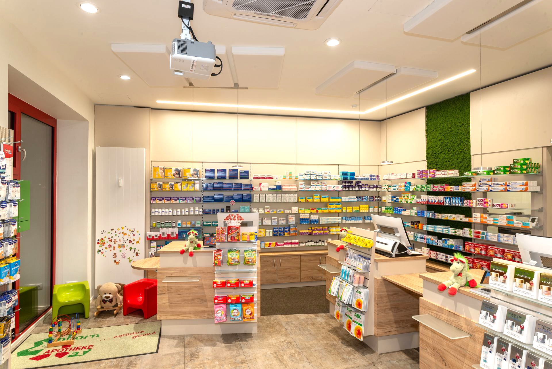 Innenansicht einer Apotheke mit Regalen voller Medikamente, Theke und Kinderspielbereich.