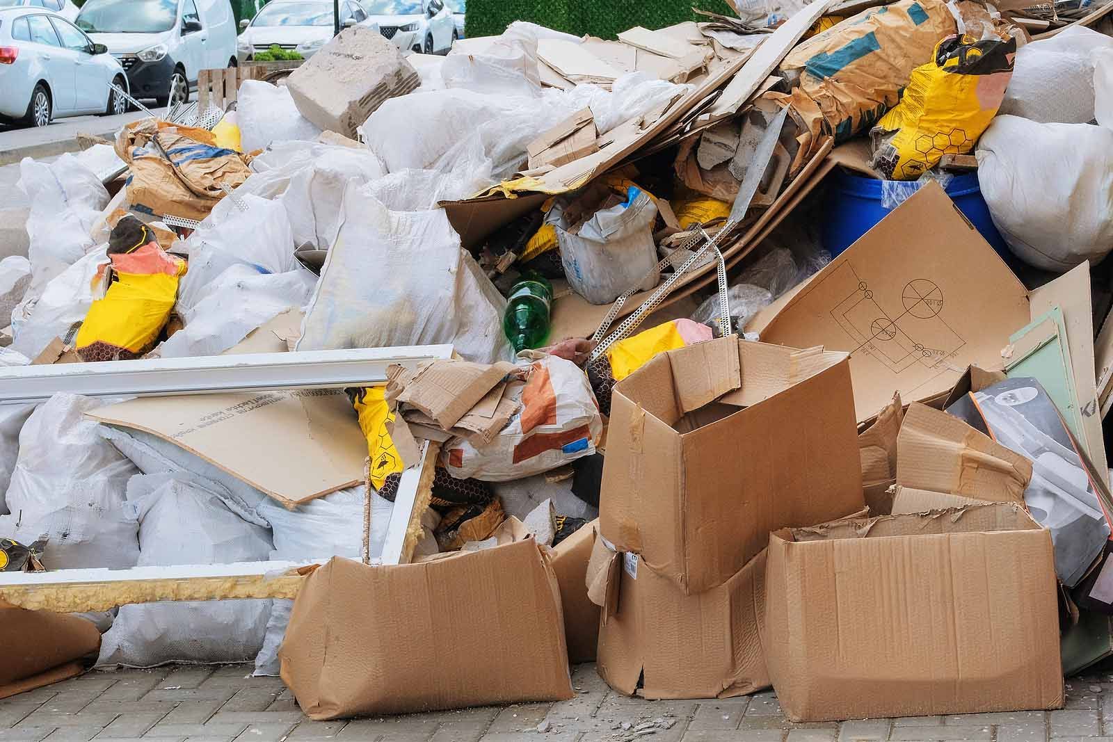Overflowing pile of mixed trash, broken furniture, and cardboard boxes on a street curb