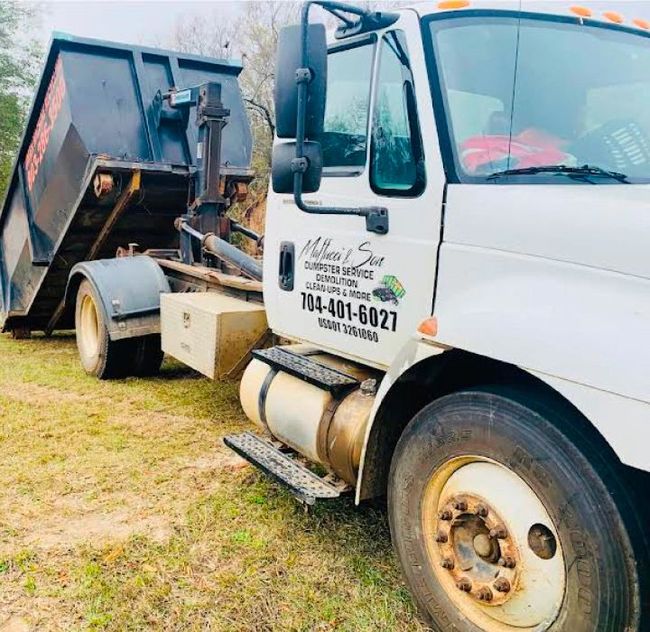 White dump truck with a raised bed parked on grass, close-up side view.
