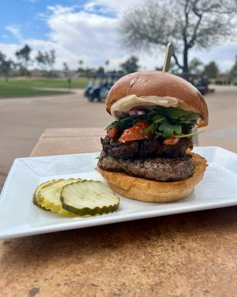 A hamburger with pickles on a white plate on a table.