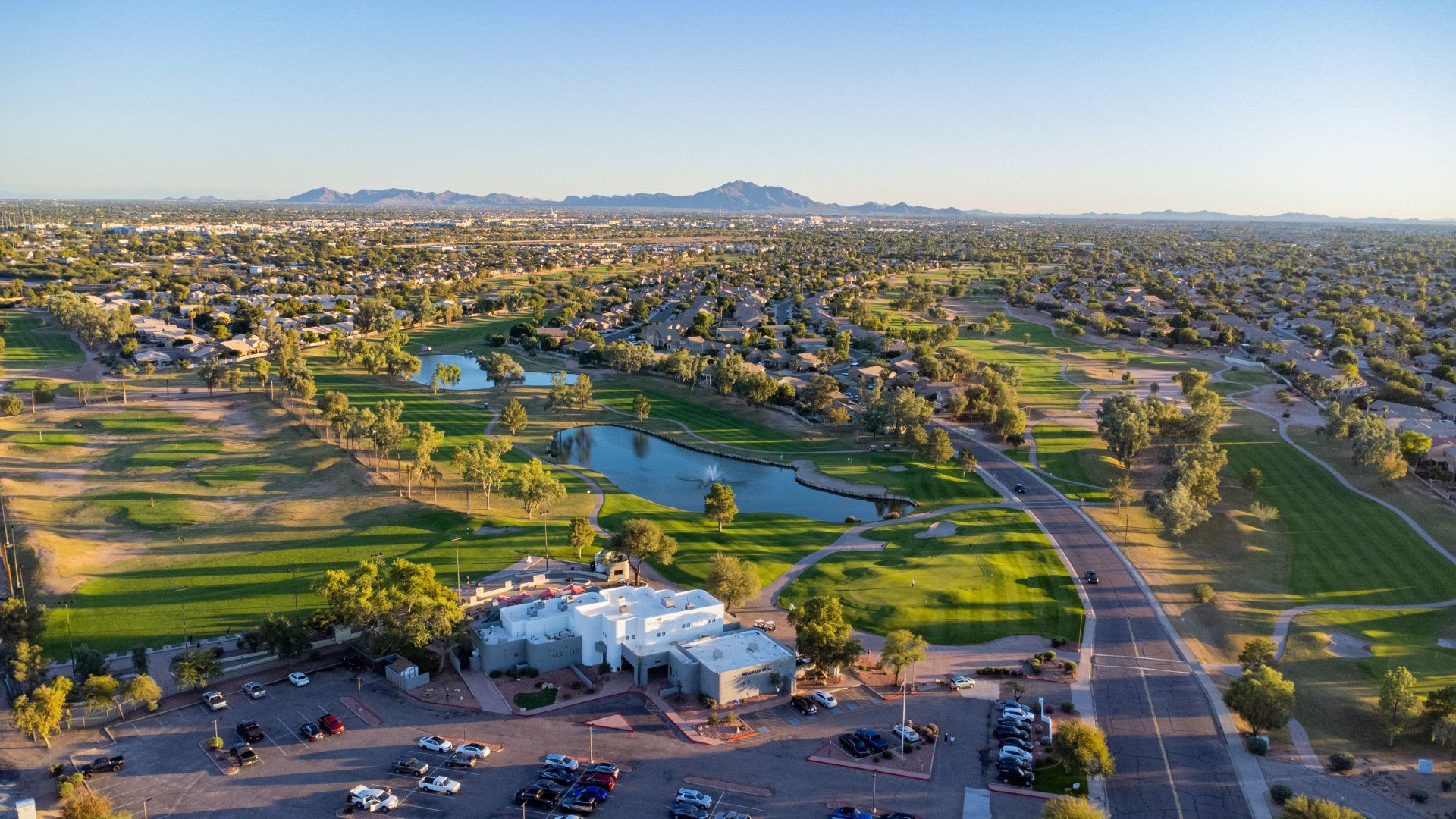 An aerial view of a golf course in the desert with mountains in the background.