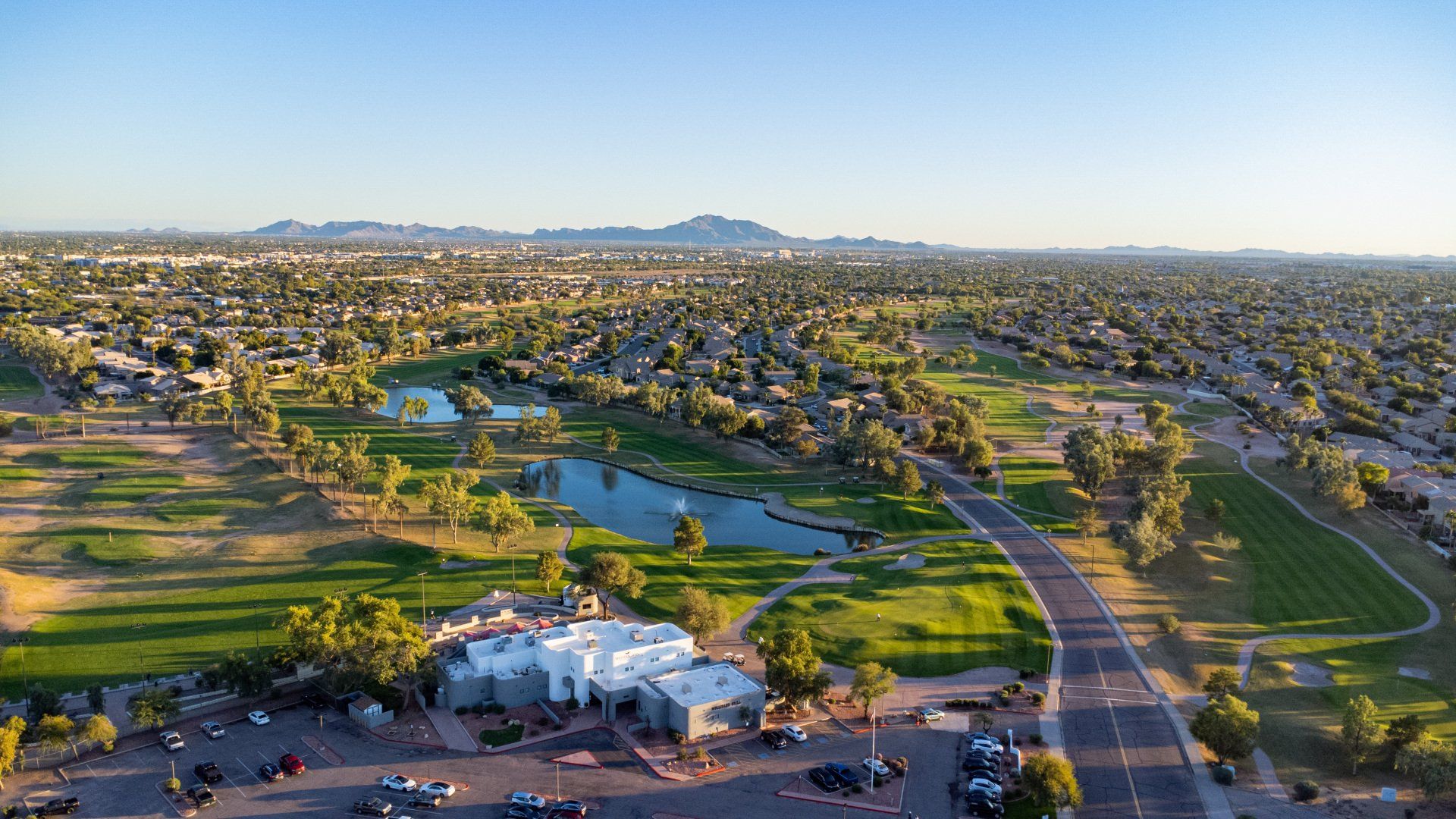 An aerial view of a golf course and a city with mountains in the background.