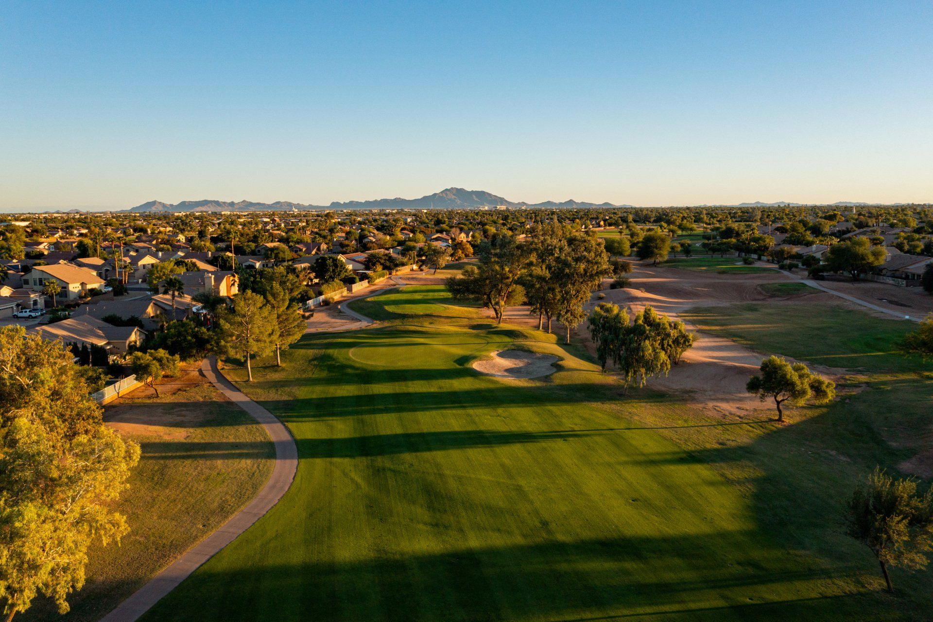 An aerial view of a golf course with trees and houses in the background.