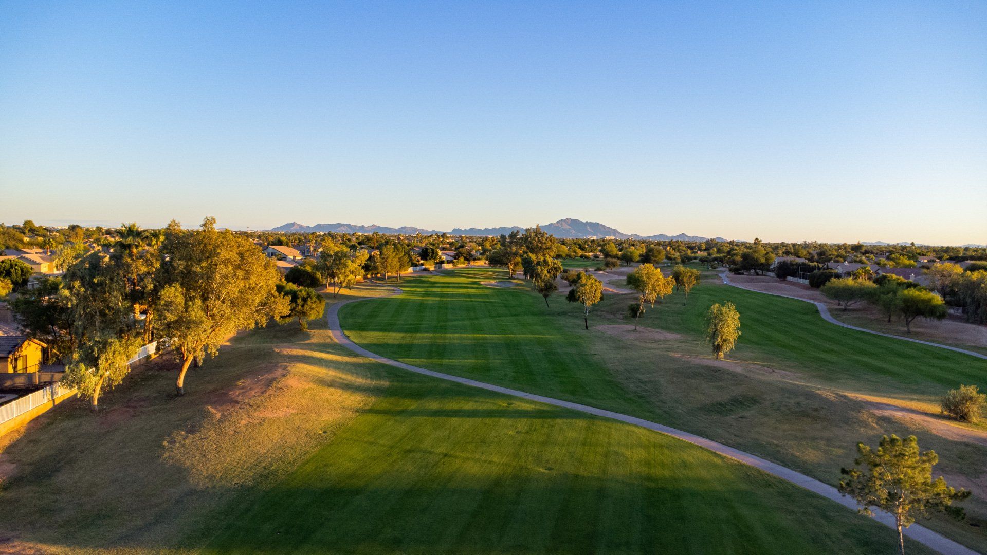 An aerial view of a golf course with trees and mountains in the background.