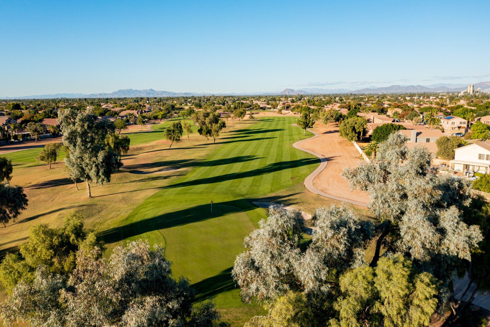 An aerial view of a golf course with trees and houses in the background.