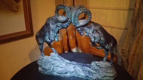 Bronze sculpture of two rams clashing horns on a rocky base.
