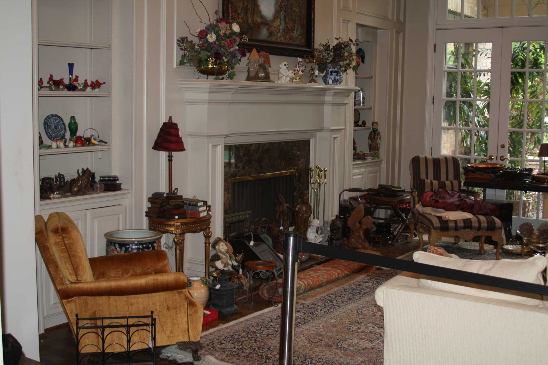 Living room with fireplace, built-in shelves, and gold armchair; French doors lead to outdoors.