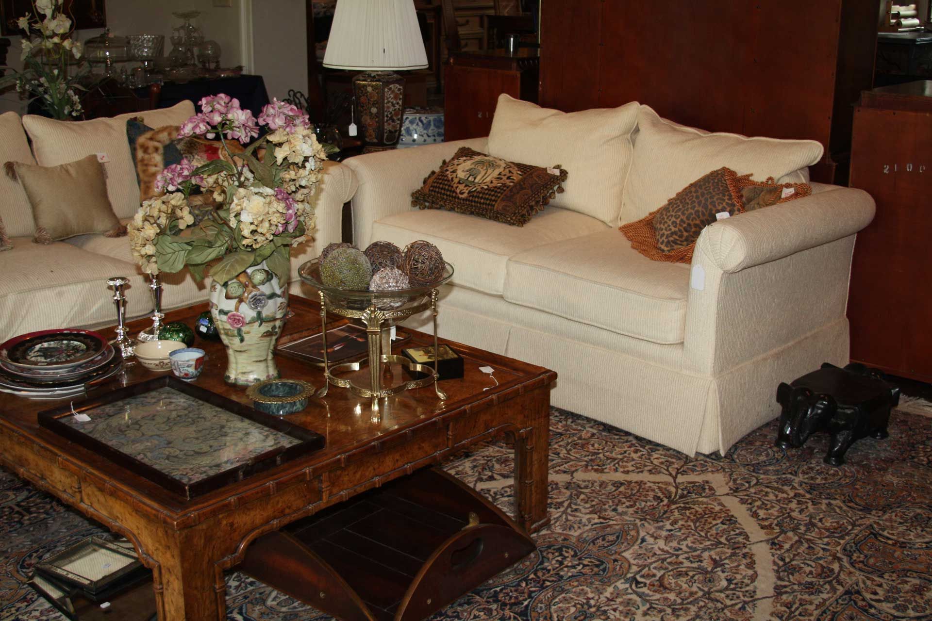 A room with furniture, including a couch, coffee table, and area rug. Flowers and lamps are present.