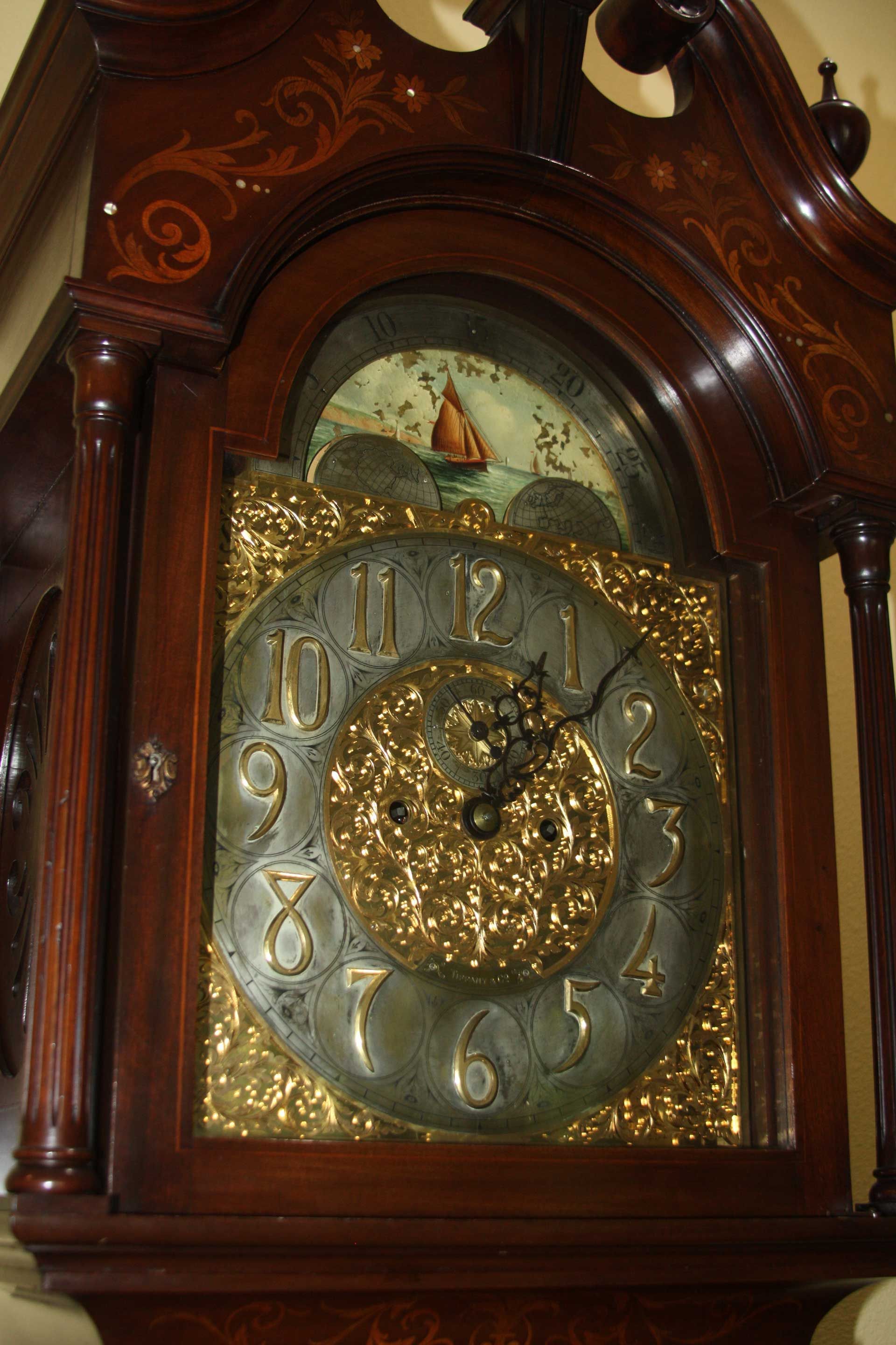 Close-up of a wooden grandfather clock with a detailed face and a painted scene above.