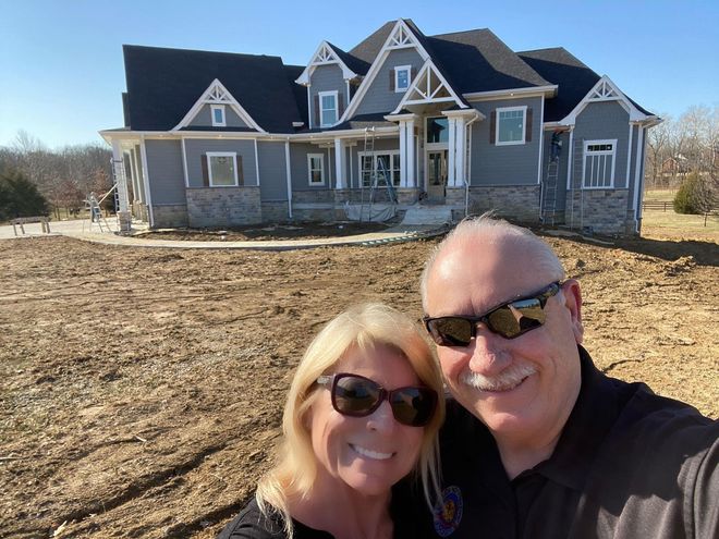 A man and a woman are posing for a picture in front of a house.