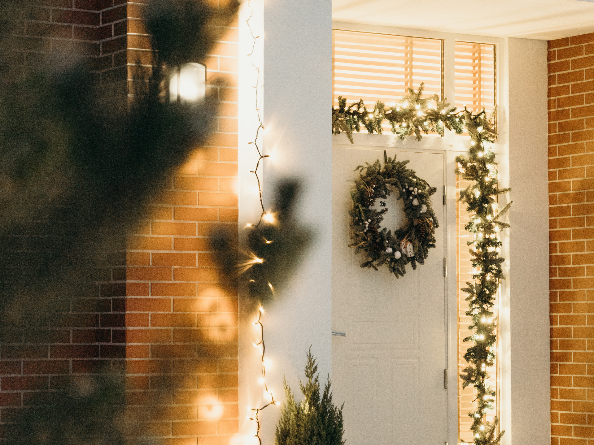 White door with a Christmas wreath and garland. Brick wall with warm light reflections.