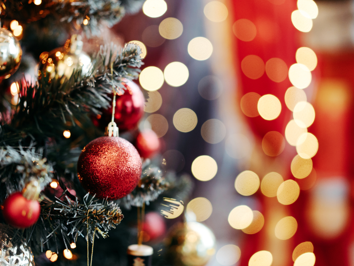 Red ornaments on a Christmas tree with blurred lights in the background.