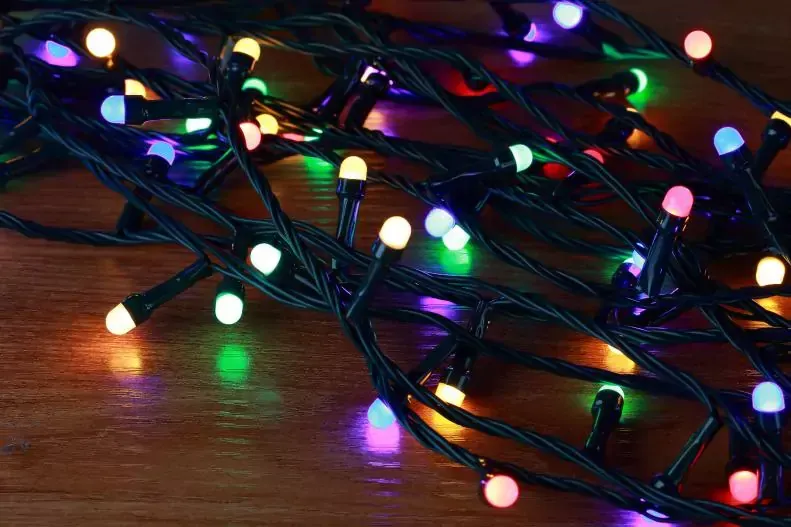 A bunch of colorful christmas lights resting on a wooden table A bunch of colorful christmas lights are sitting on a wooden table.