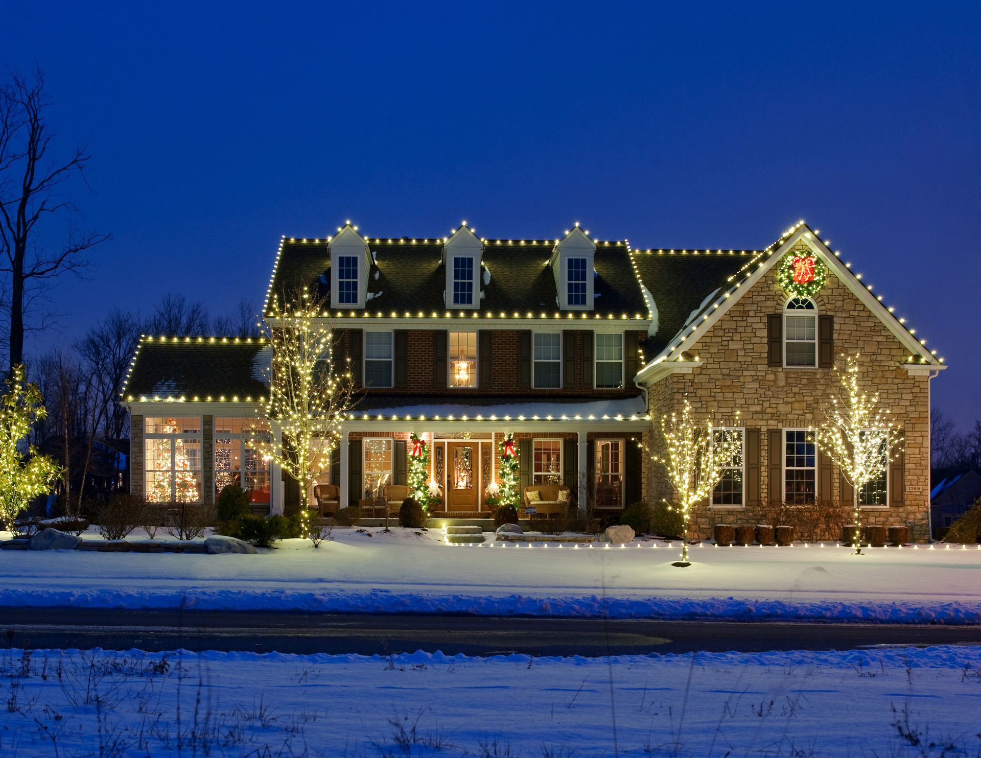 House decorated with white Christmas lights against a dark blue sky and snow.