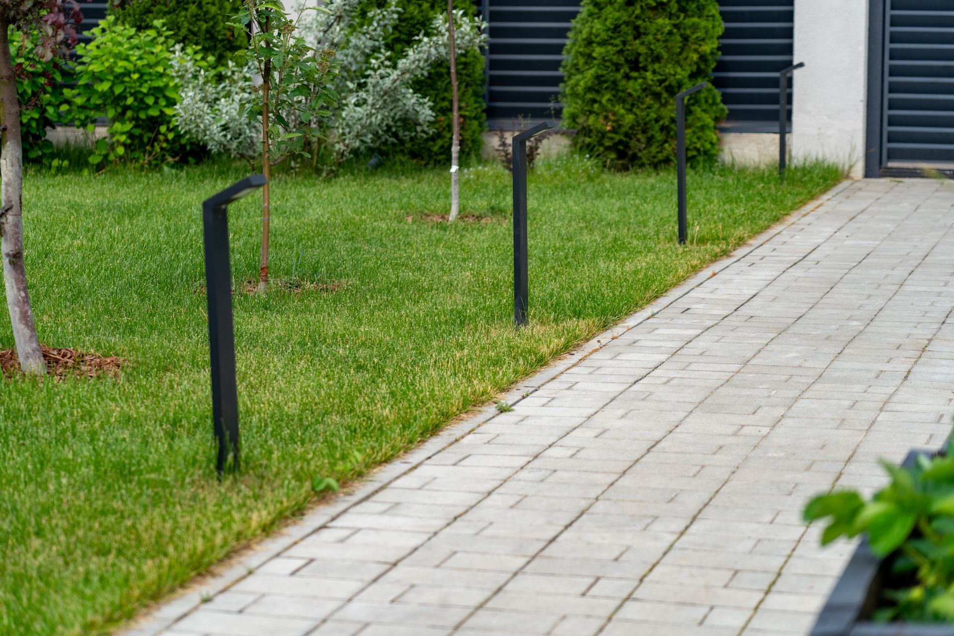 Grassy sidewalk edge with black posts and a paved path beside apartment buildings