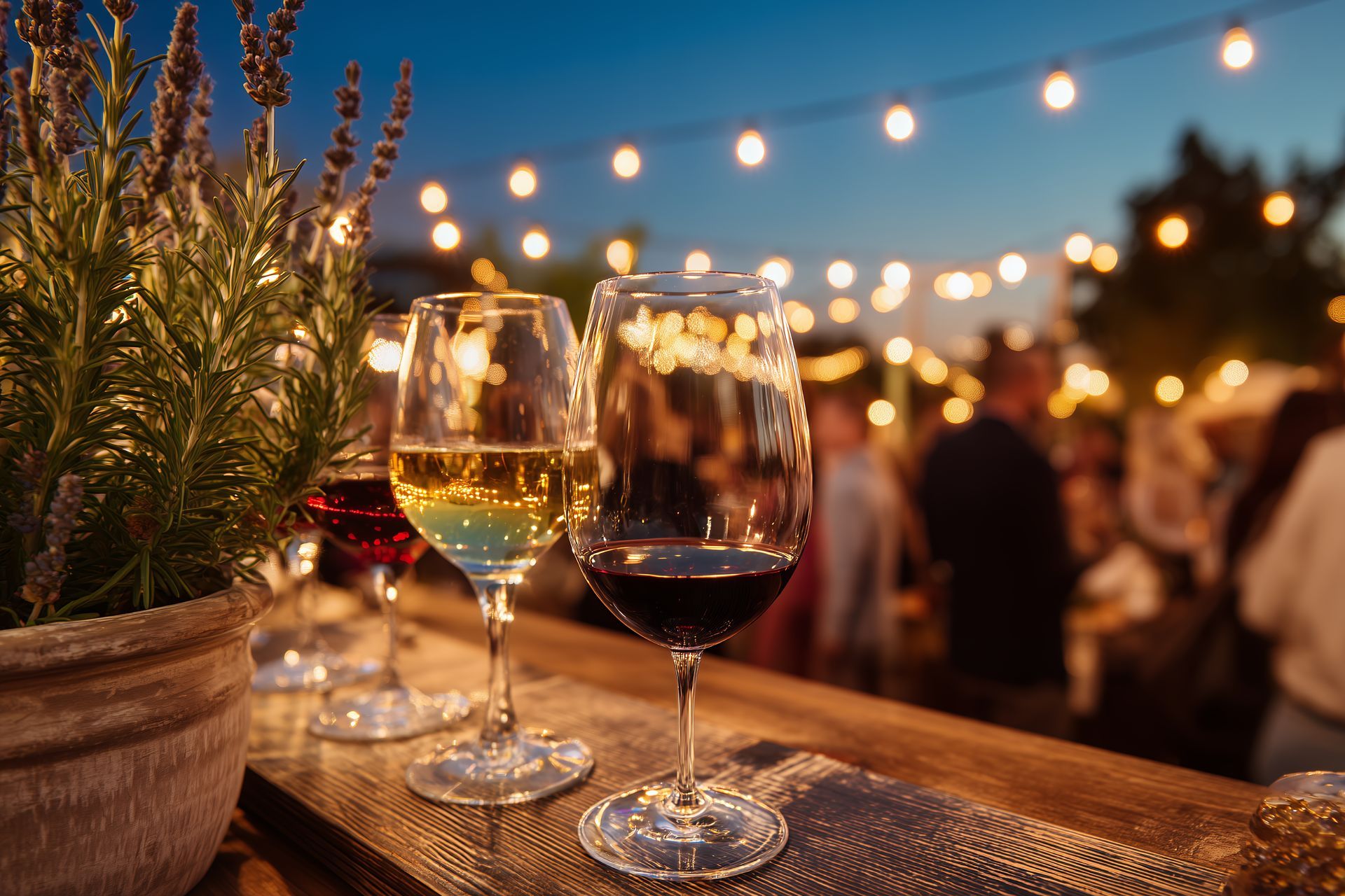 Wine glasses on a wooden table at an outdoor evening gathering with string lights and blurred guests