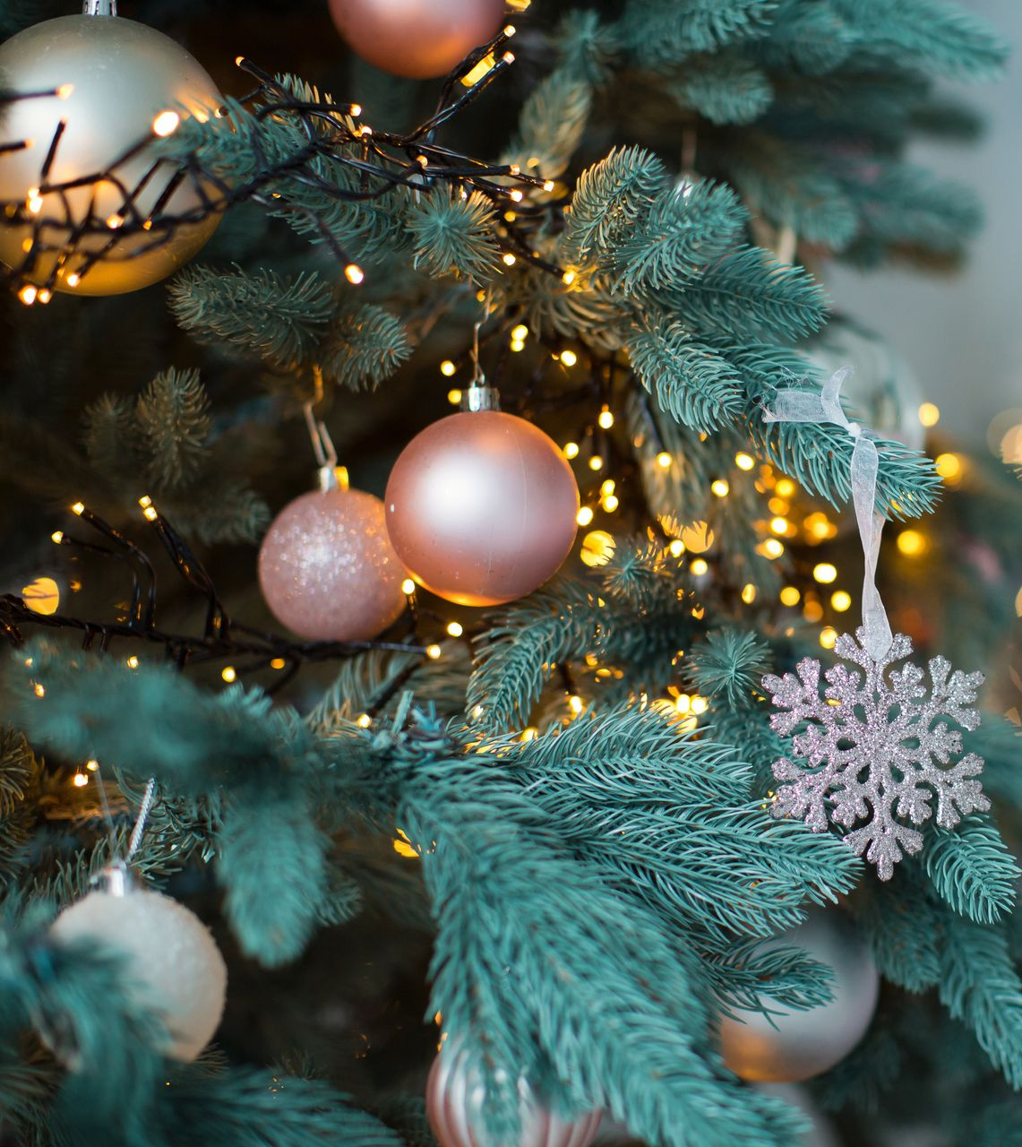 Red Christmas ornaments on a decorated evergreen tree with bokeh lights, snowflakes.