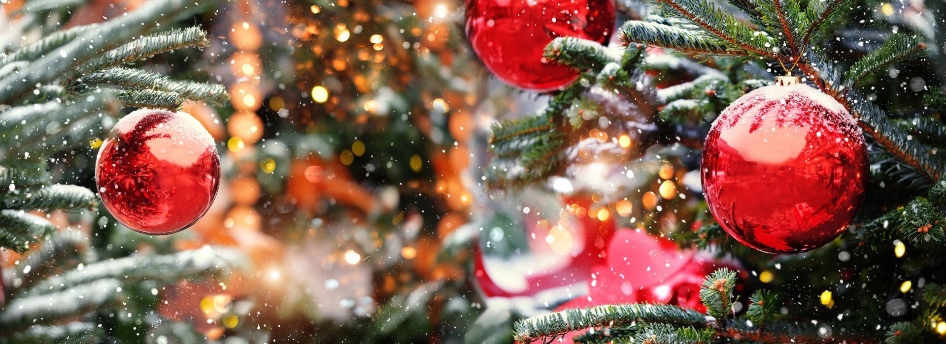 Red Christmas ornaments on a decorated evergreen tree with bokeh lights, snowflakes.