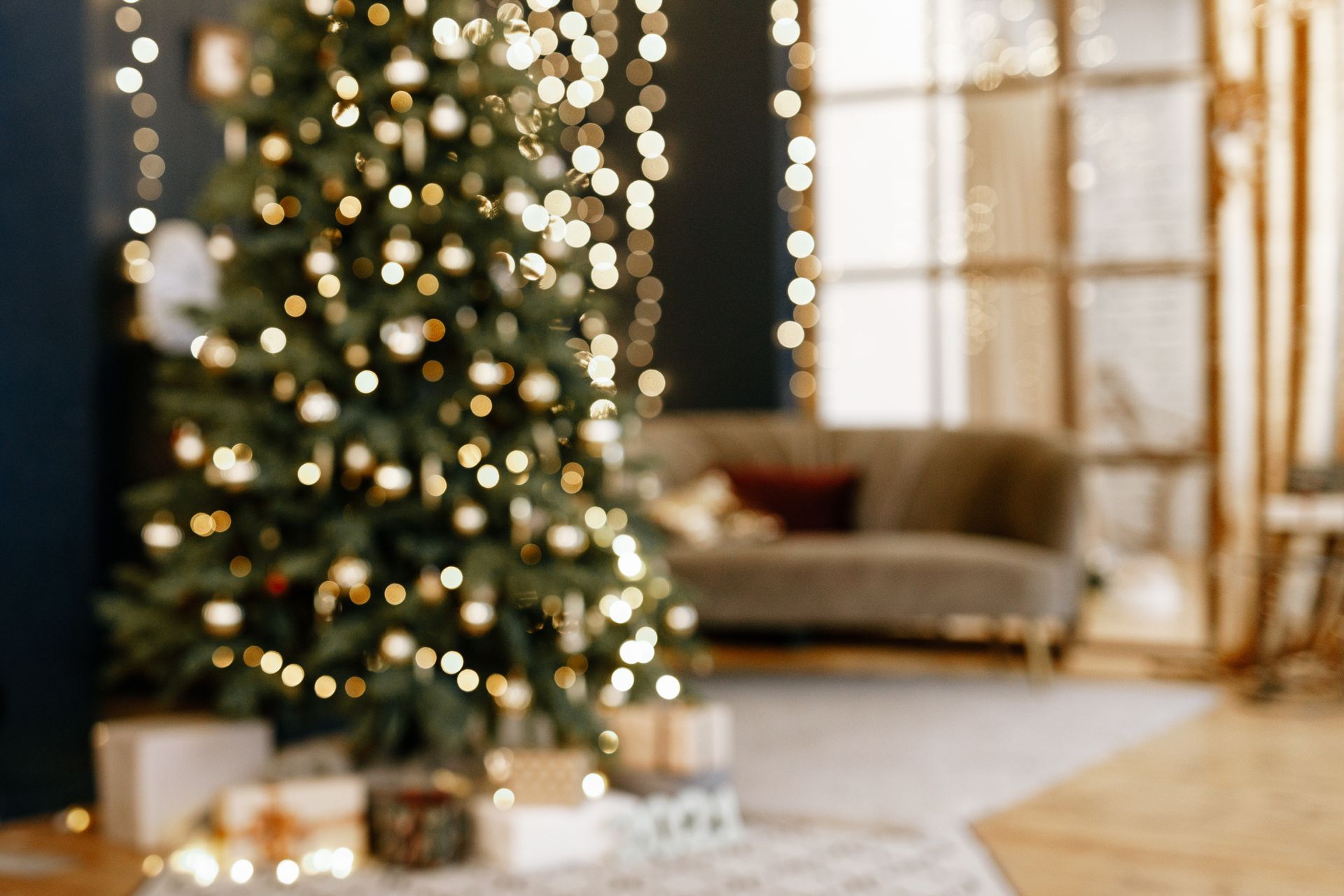 A cozy porch decorated for Christmas with a lit tree, a wreath on the door, and numerous candles glowing on the floor.