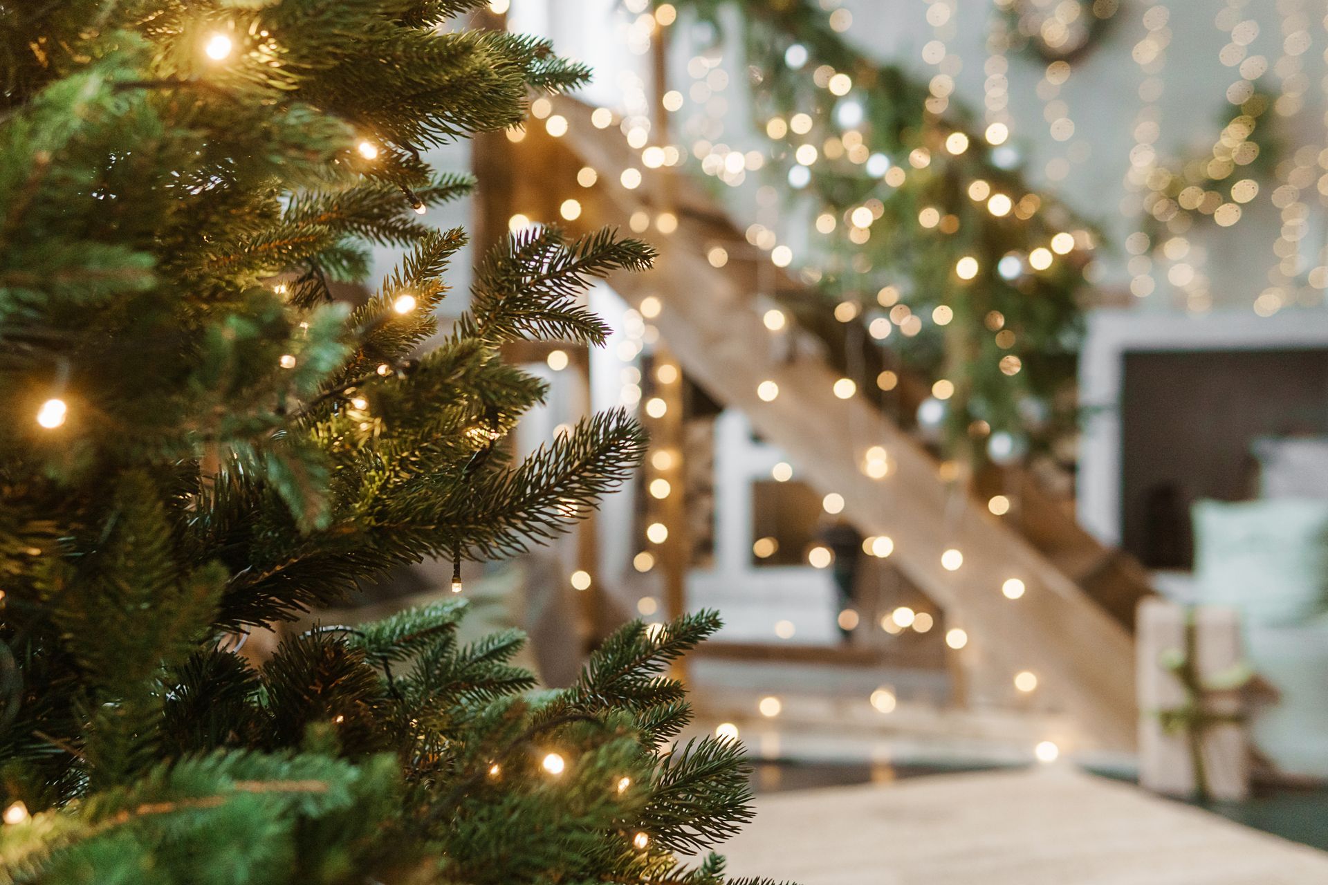 A cozy porch decorated for Christmas with a lit tree, a wreath on the door, and numerous candles glowing on the floor.