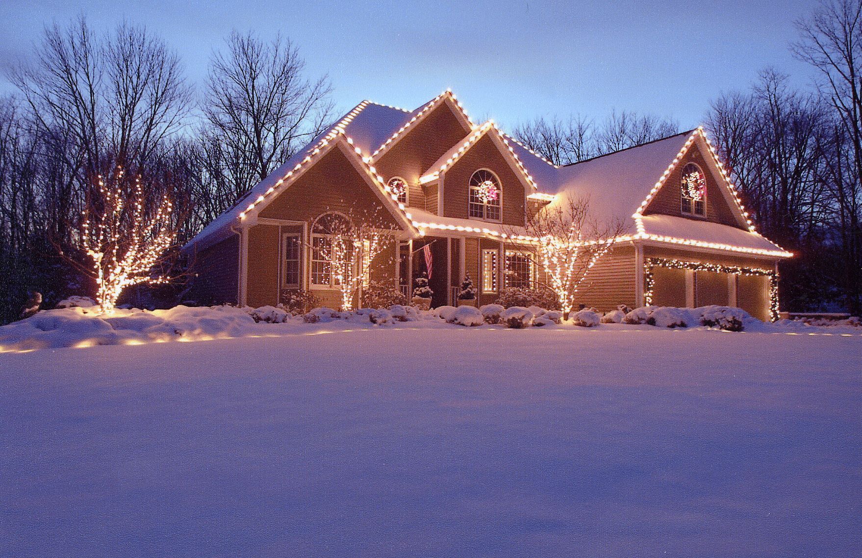 Snowy house with Christmas lights glowing at dusk.