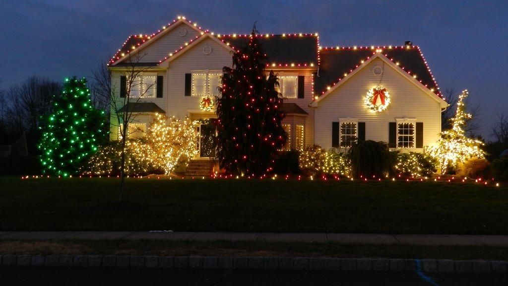House decorated with Christmas lights: green, gold, and red on the house and surrounding bushes.