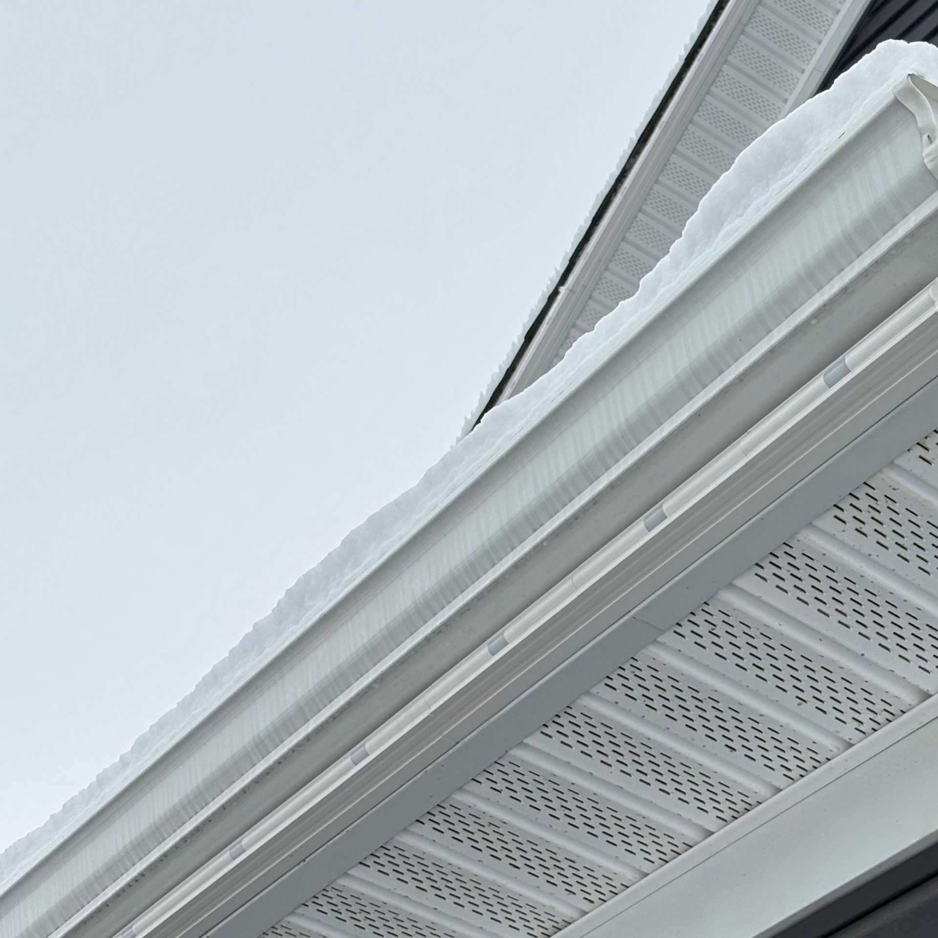 Snow-covered house roof and white gutter against a pale sky
