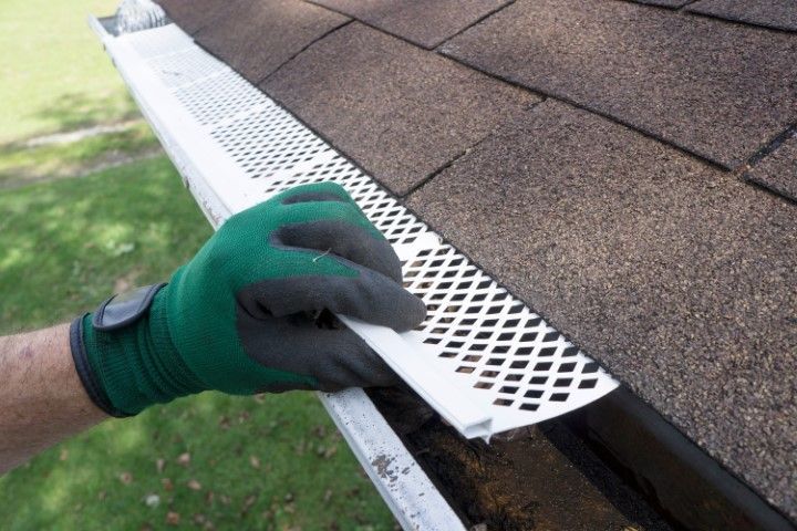 Gloved hand installing a white gutter guard along a shingled roof edge