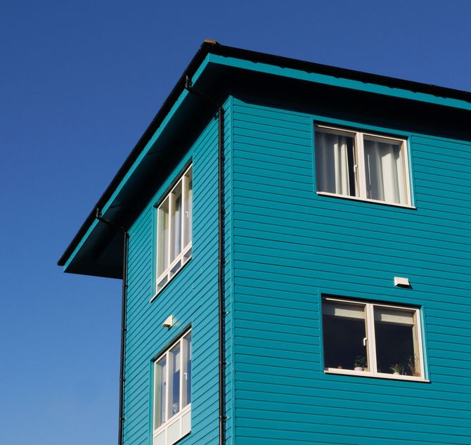 Turquoise apartment building corner with white-framed windows against a blue sky