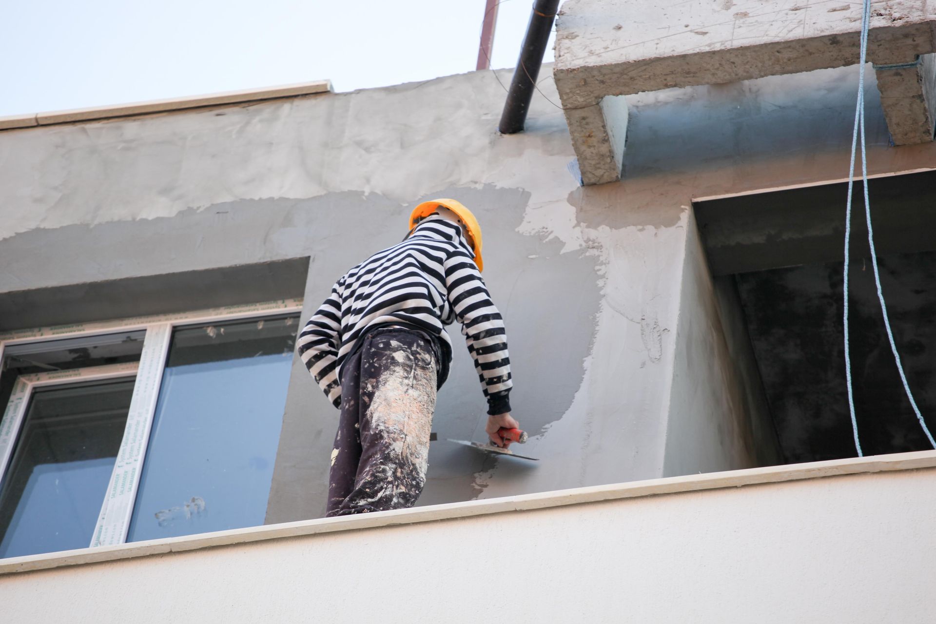 Construction worker in hard hat, applying cement to exterior wall with a trowel.