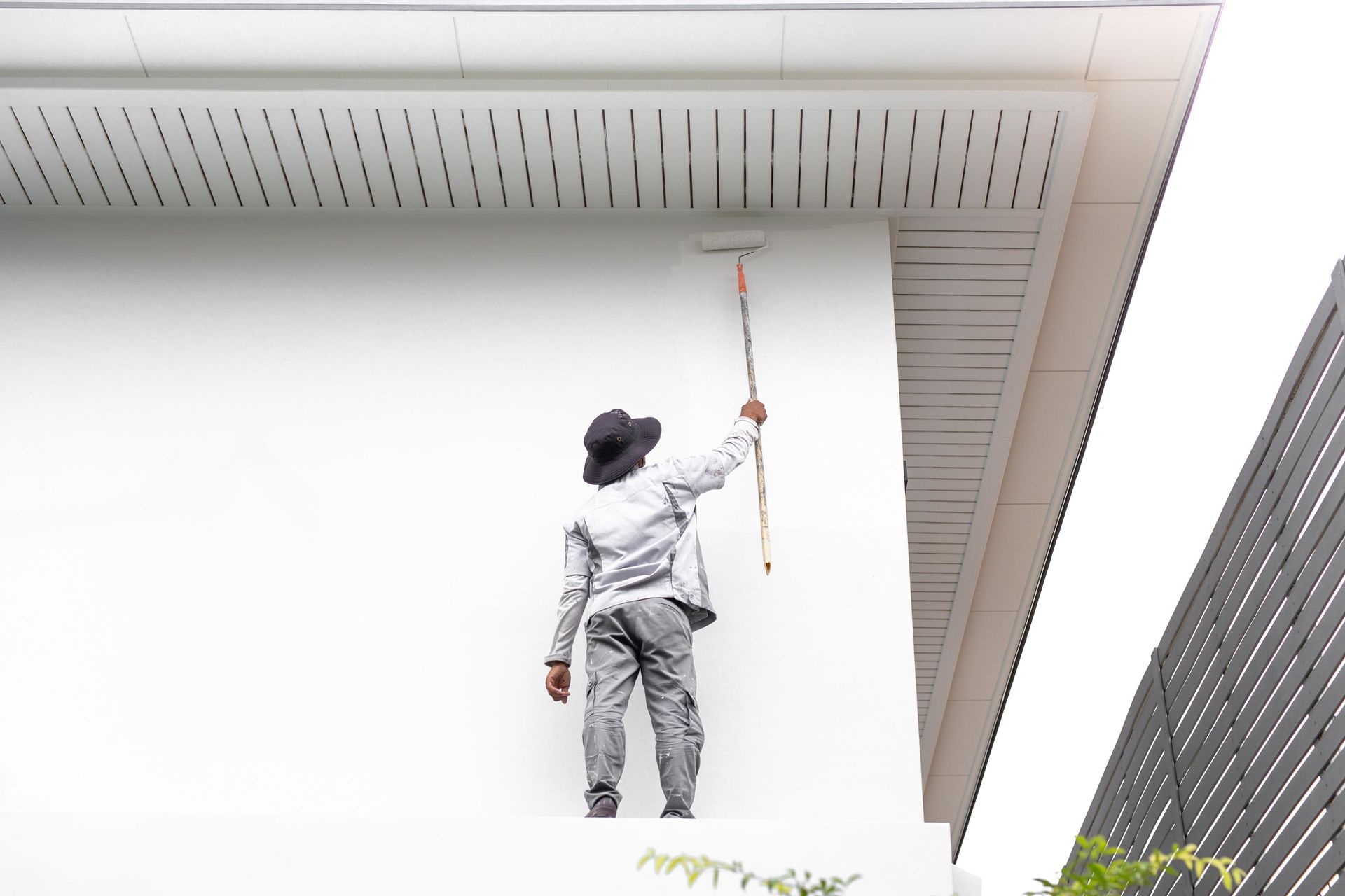 Person painting a white wall of a building with a roller.